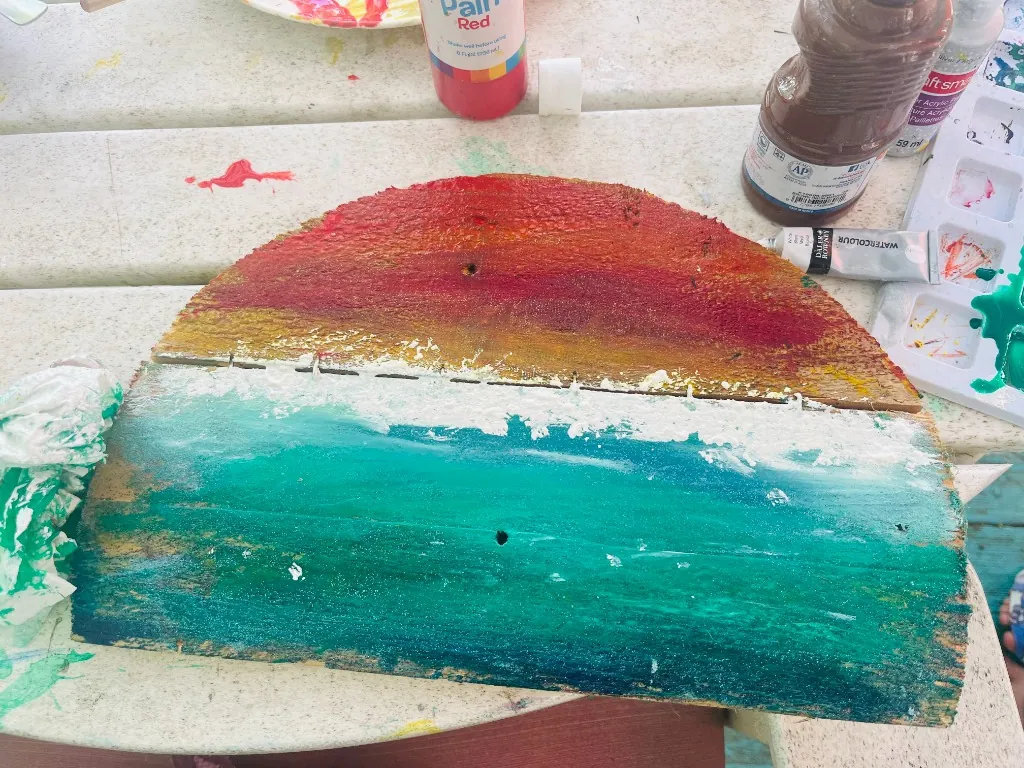 A wooden board painted with a vibrant sunrise over the ocean