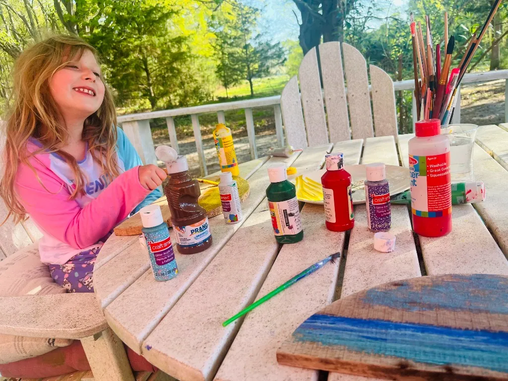 A young girl at a painting table with many supplies