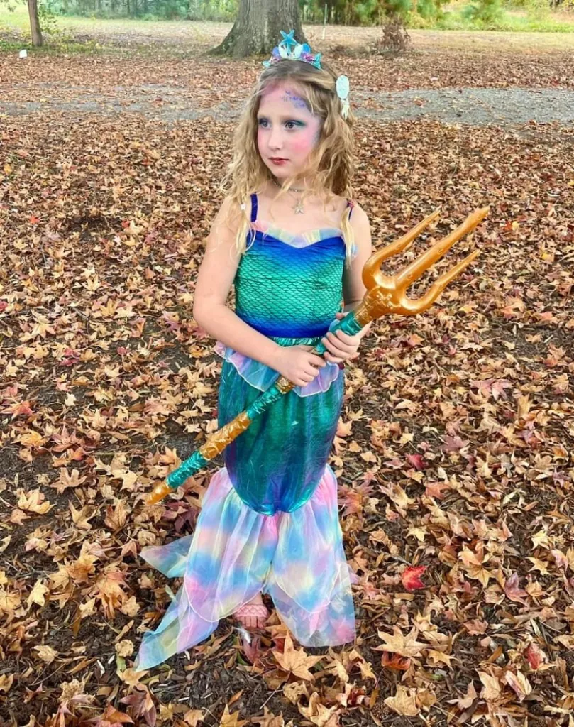 A young girl dressed as a mermaid with a gold trident